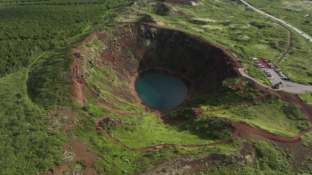 Een weids uitzicht op de Kerið-krater in IJsland, die de weelderige groene vegetatie, rode vulkanische aarde en kronkelende paden naar de locatie toont.