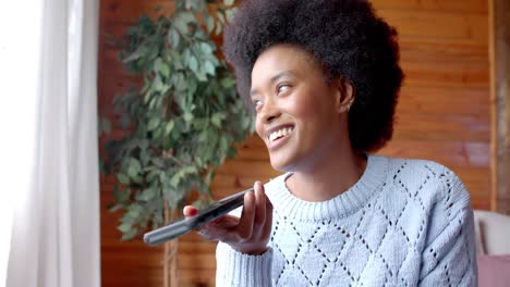 happy african american woman talking on smartphone and drinking tea in living room, in slow motion