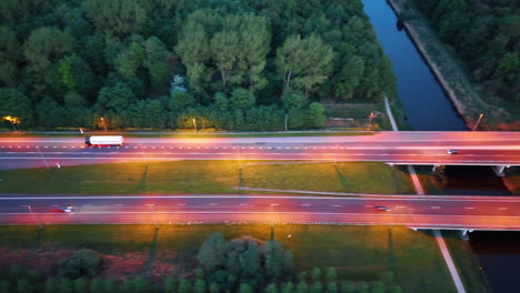 cars move by the roads illuminated pink at dusk time. flight over the canal and forest. the netherlands.