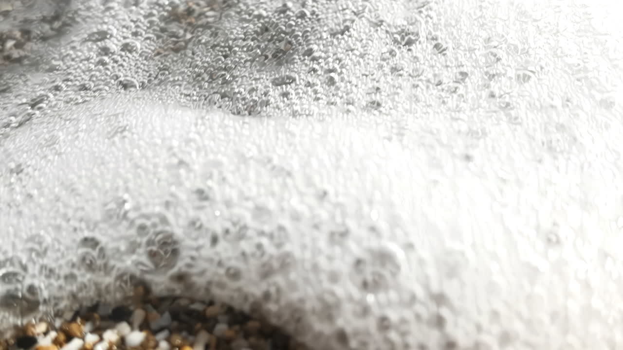 Slow motion footage of sea splashing on shells and pebbles