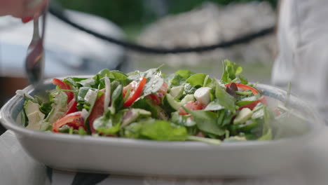 a caucasian woman tossing a fresh green salad outoors - handheld close-up