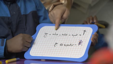 a teacher helping a young students with arabic letters