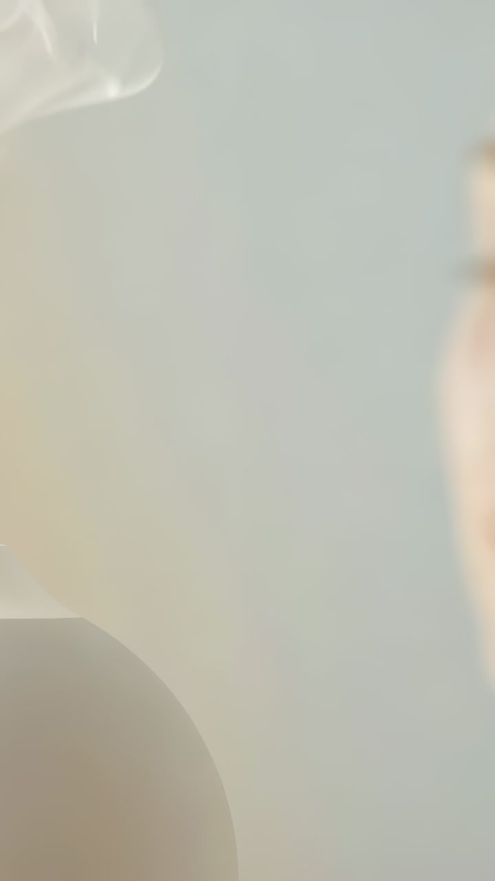 Vertical video: Camera zoom drawing woman leaning cheek toward jar in studio, copy space