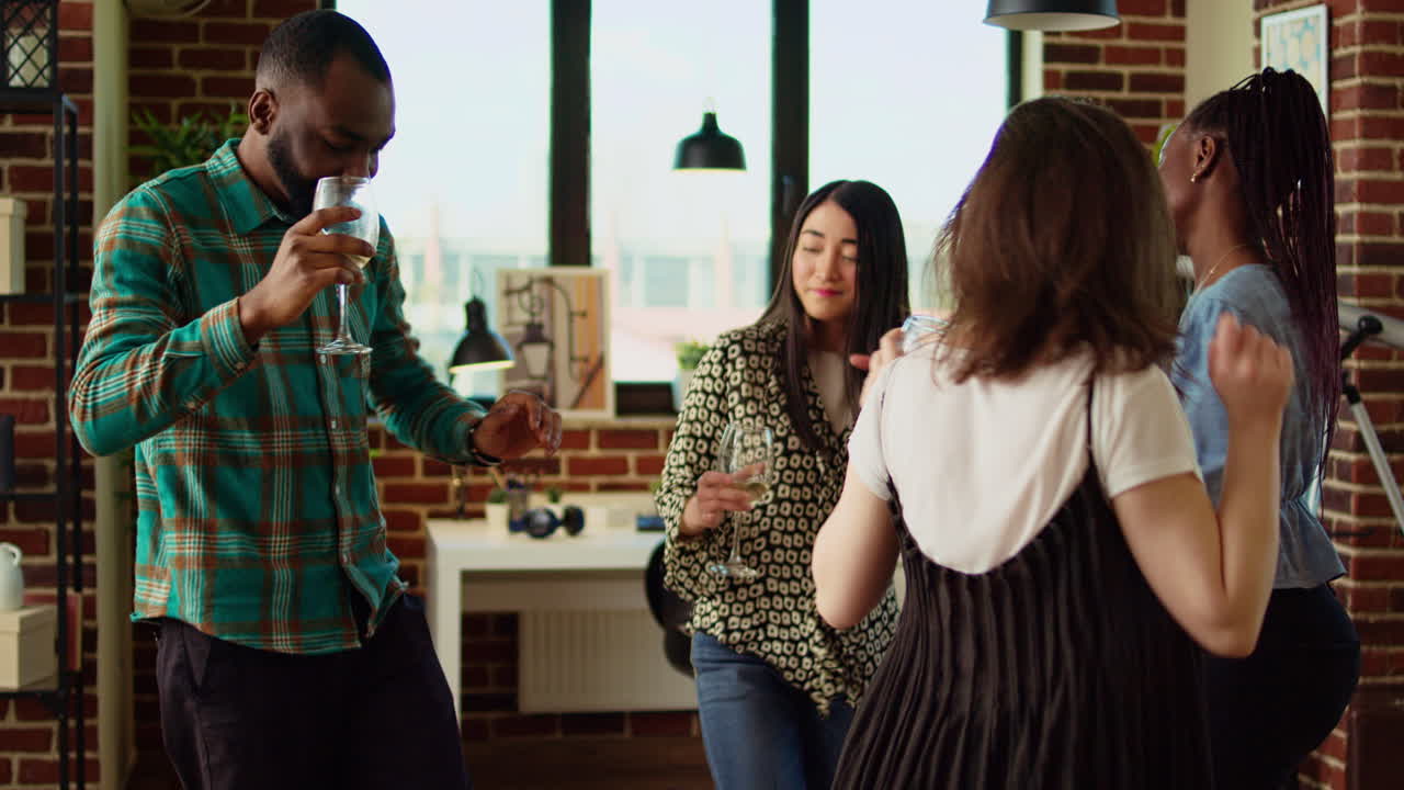 BIPOC group of young adults dancing at apartment party while drinking wine glasses