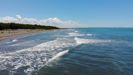 onde del mare che spumeggiano verso la spiaggia sabbiosa in una bella giornata di sole con nuvole bianche sul cielo blu nel mediterraneo