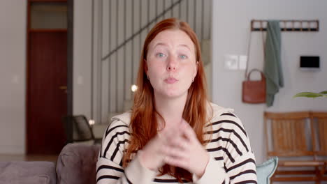 talking and gesturing, woman with red hair in casual striped shirt indoors, video call