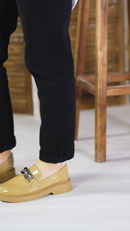female walking back and forth in fashionable new shoes. beige stylish footwear on plain soles with chain decoration. wooden stool and folding screen at backdrop. vertical video