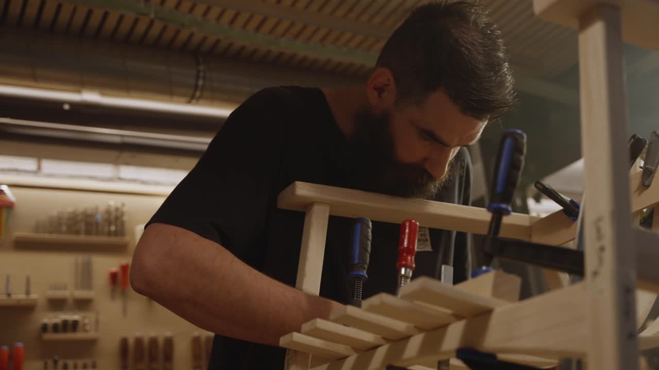 Focused craftsman assembling a wooden chair frame using clamps in a woodworking workshop, symbolizing precision, handmade furniture craftsmanship, and attention to detail