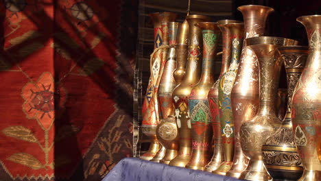 row of ornate gold plated vases lined in market next to handmade rug in yerevan, armenia