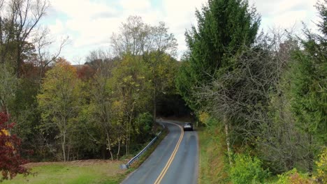 small sport utility vehicle suv driving down winding hill into woods during autumn