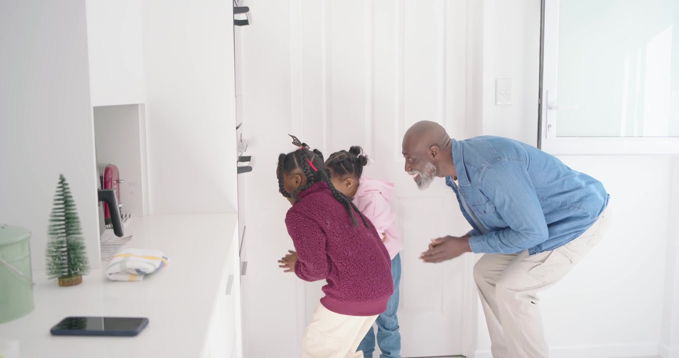 African family man guiding 2 children sliding cookie tray into oven in white kitchen baking cookies