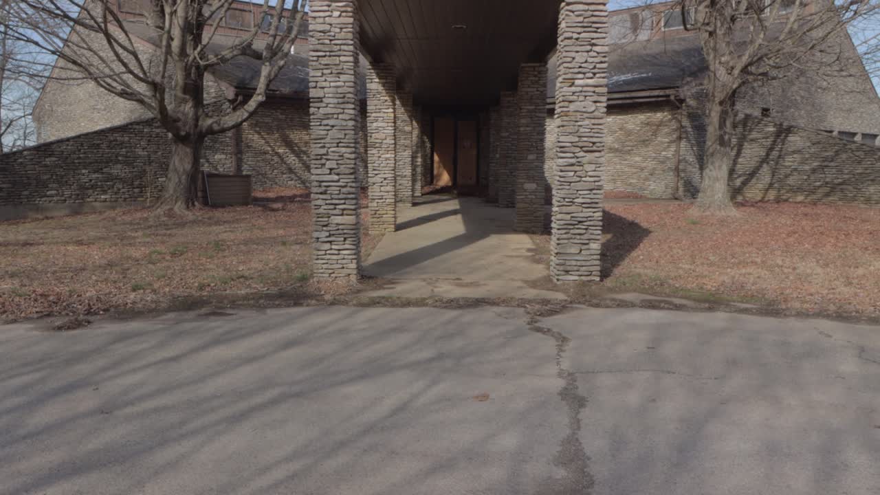 The Covered Walkway to the Boarded-up Entrance to an Abandoned Lodge.  Static Shot Showing the Walkway, Building, Fallen Leaves, and the Boarded Doors