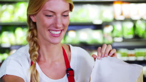 female staff packing fruits in paper bag at supermarket