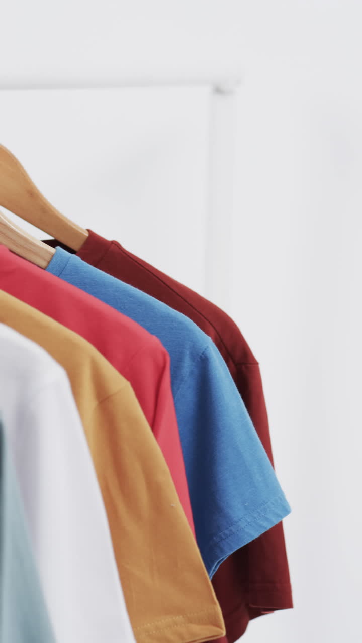 Vertical video of three multi coloured t shirts on hangers and copy space on white background