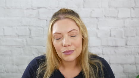 a pensive thoughtful blonde woman staring into space deep in thought thinking with a white brick wall background