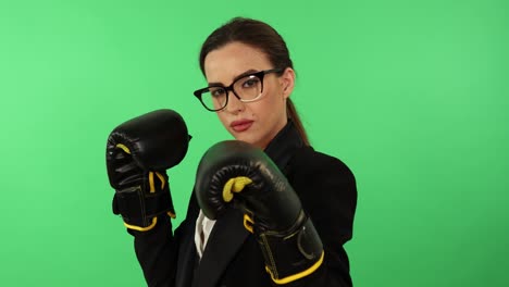 mujer de negocios con gafas y cola de caballo con camisa blanca y atuendo de negocios negro usa guantes de boxeo para golpear hacia la cámara