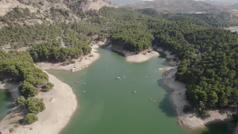 drone view of la isla el chorro featuring small boats surrounded by aromatic pine forest of the malaga lake district in andalusia spain