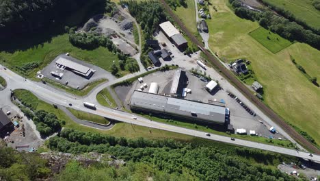 Flying-over-the-edge-of-high-cliff-watching-Norwegian-highway-E-16-and-industrial-area-Dalegarden-far-down-below---Spectacular-aerial-with-traffic-on-road-below