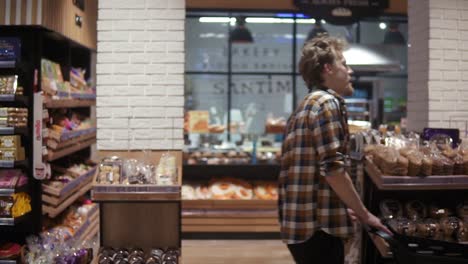 Shopping-in-the-supermarket,-side-view-of-the-male-customer-walk-happily-the-trolley.-A-guy-pushing-shopping-cart-by-the-supermarket-aisle