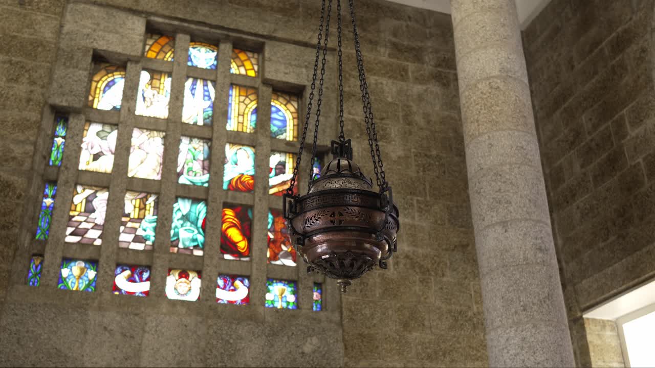 Metal thurible suspended beside stained glass window in stone walled church interior