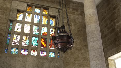 metal thurible suspended beside stained glass window in stone walled church interior