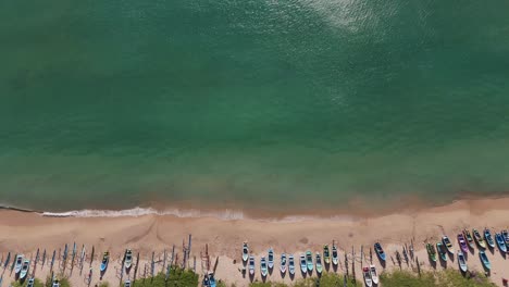 green blue wave formations lapping the white sandy shoreline with fishermen’s boars ontrincomalee beach, sri lanka. aerial static .