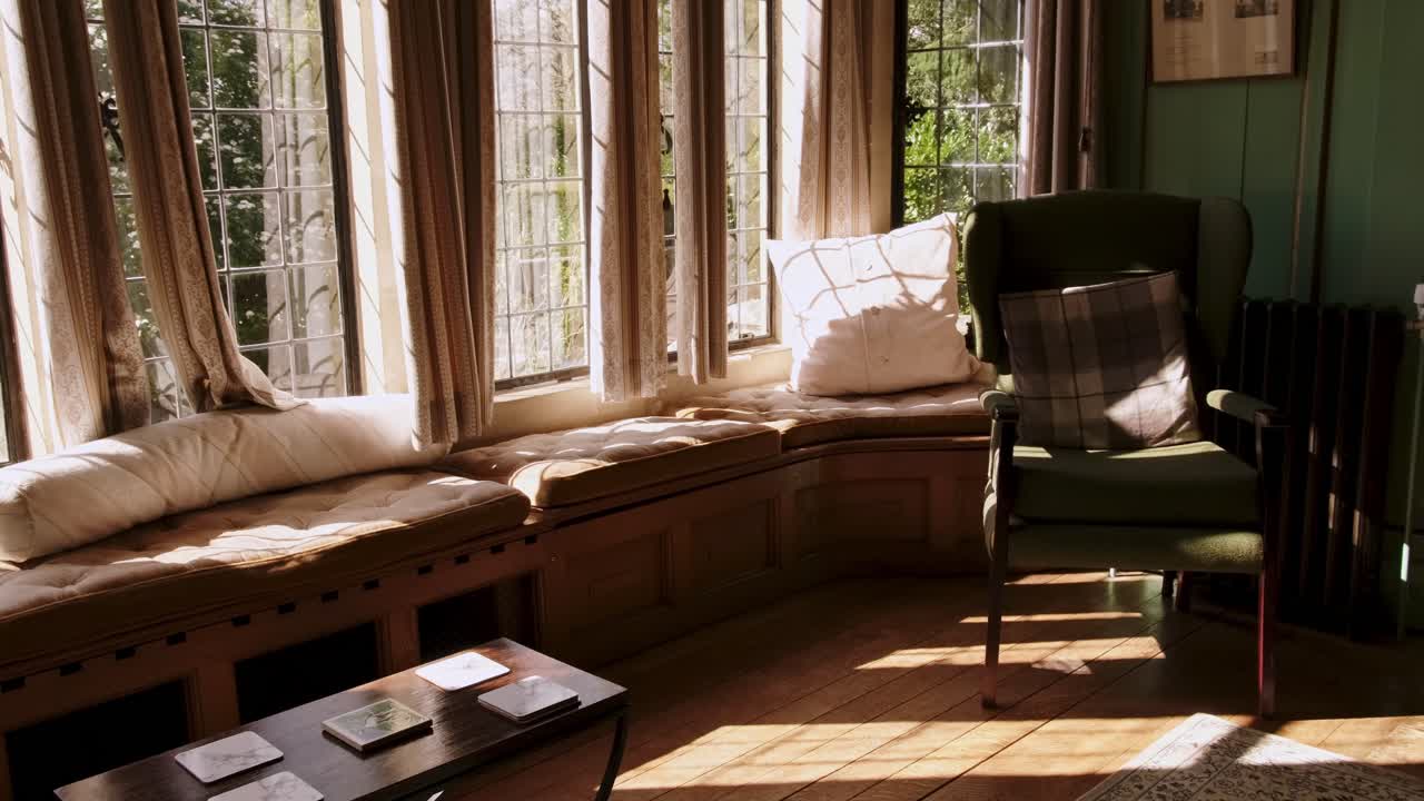 Cinematic shot of inside mansion living room with casual decor and soft lighting from windows.