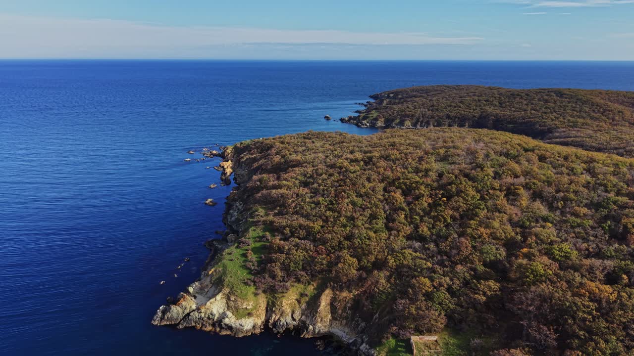 Coastal cliffs meet tranquil blue waters in serene aerial view
