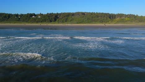 aerial shot gliding over ocean waves in the pacific ocean and beach in ocean shores
