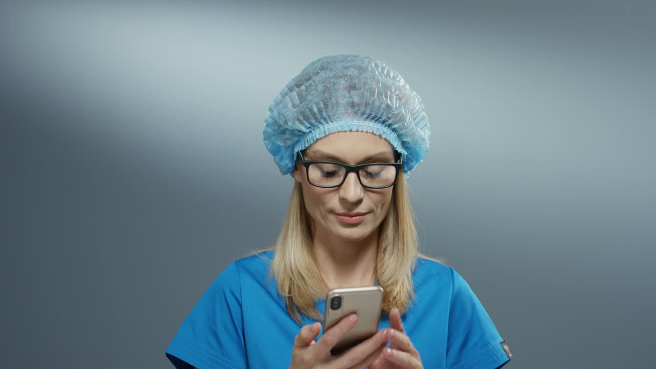 Attractive Young Female Medic In Blue Costume, Hat And Glasses Speaking Cheerfully On The Phone And Smiling