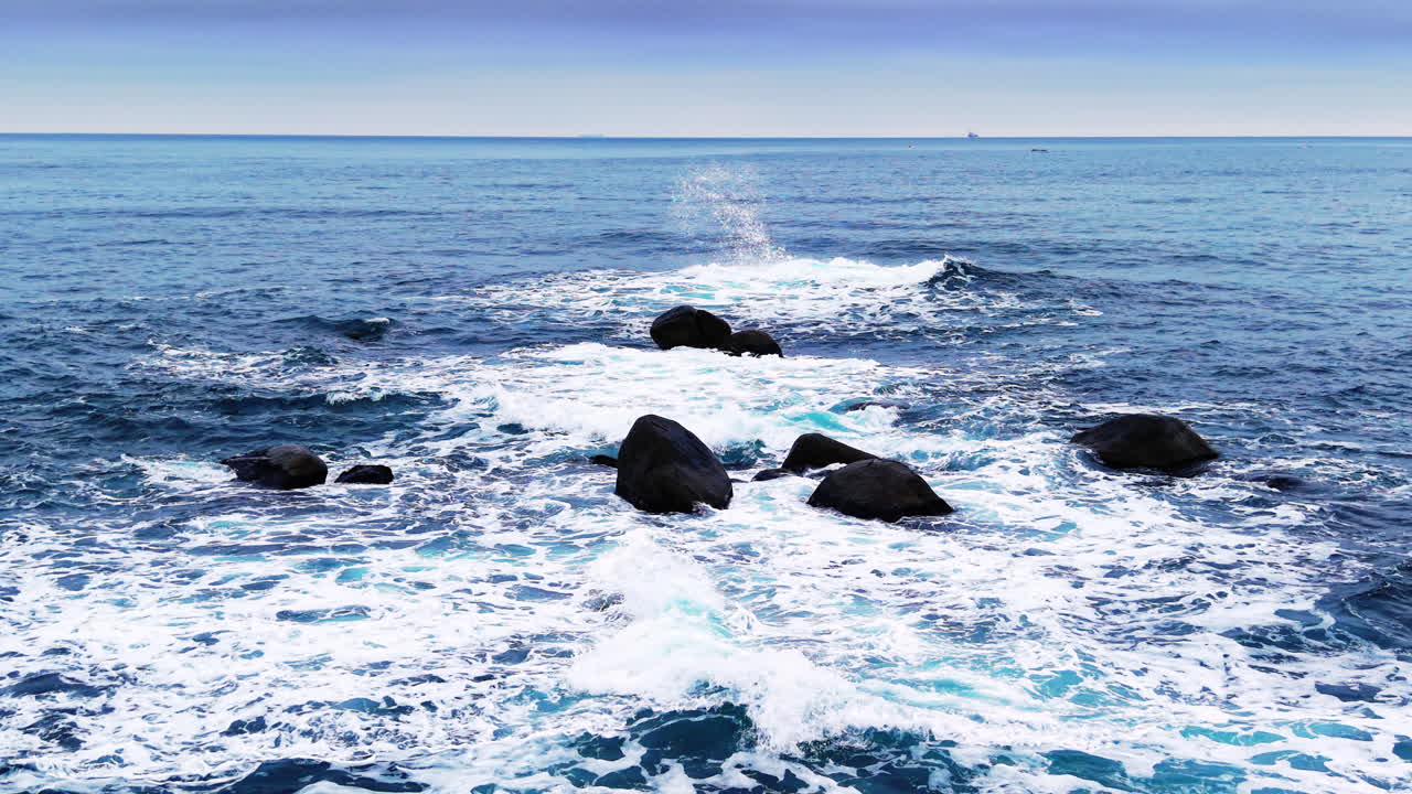 Massi scuri che affiorano dall'oceano con schizzi d'acqua e schiuma di mare bianca. Rocce nere nel mare con onde bianche che si infrangono. Vista aerea.
