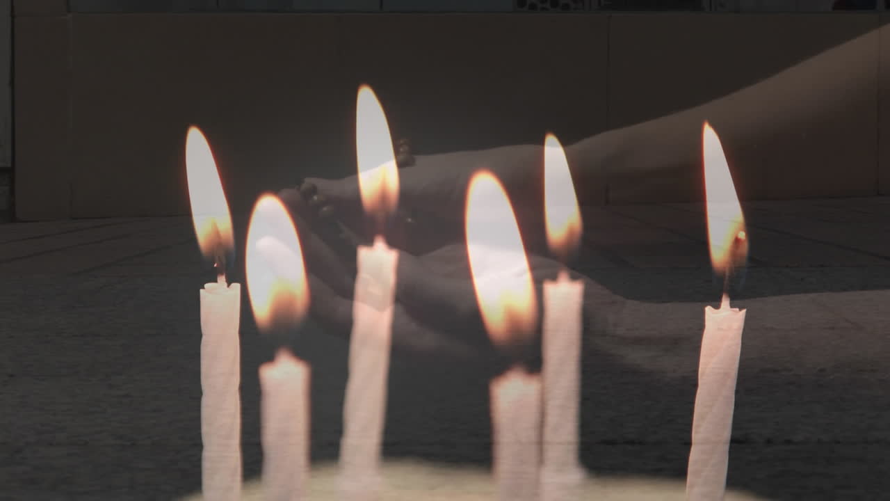 Video composito di candele che si spengono sulle mani di una donna che prega con il rosario, sullo sfondo di persone che camminano