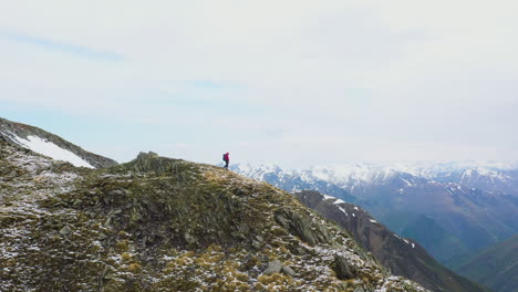 Drone-shot-of-hiker-standing-on-top-of-a-mountain-ridge-in-the-snow-covered-Caucasus-Mountains-in-Georgia