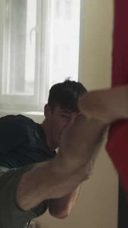 el entrenador del hombre sostiene el equipo de lucha libre mientras el tipo enfocado patea el objetivo. trabajando con un experto en el sótano del club deportivo. ganando energía haciendo ejercicios
