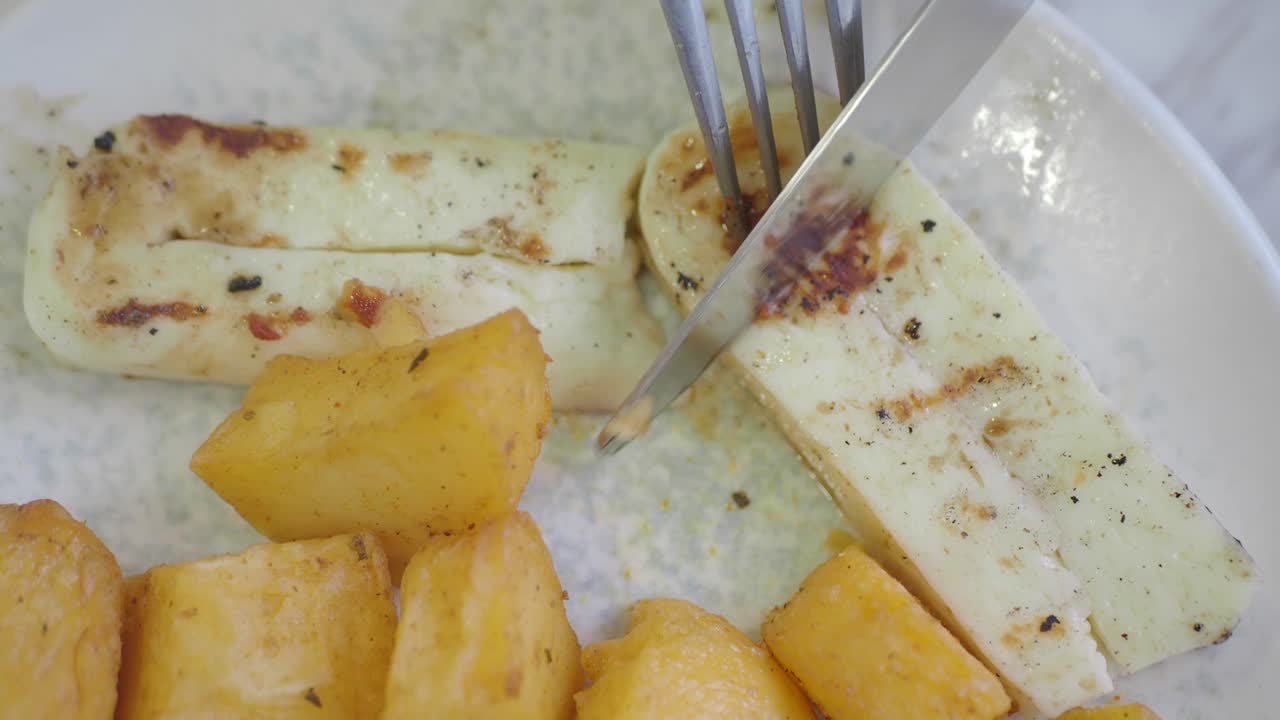 Close-up of cutting grilled cheese and roasted potatoes on a plate
