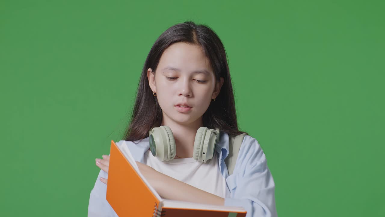 녹색 스크린 배경 스튜디오에 서서 책을 읽는 배을 가진 피곤한 아시아 십대 소녀 학생의 클로즈업