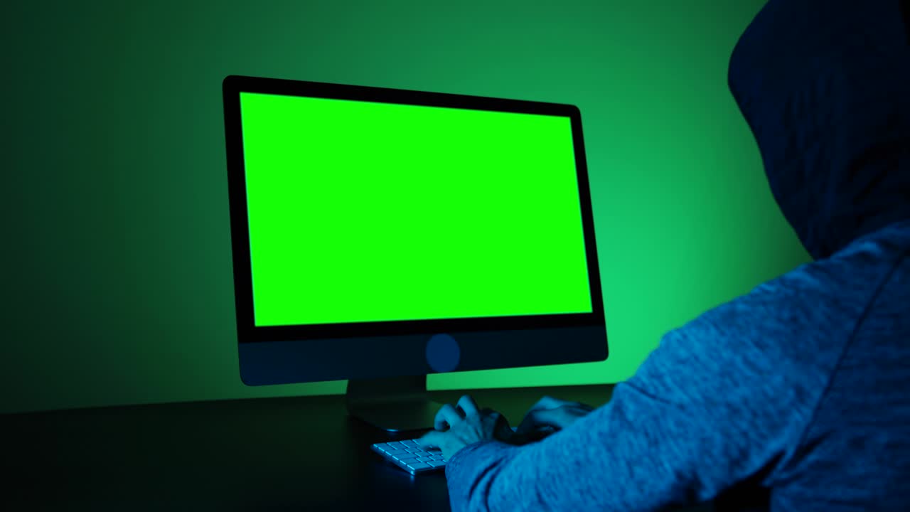 un hombre irreconocible hackeando en una habitación oscura con pantalla verde.