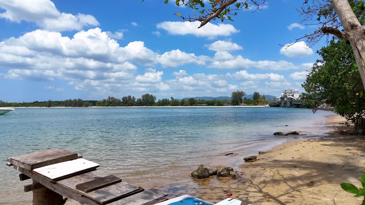 imágenes aéreas de una tranquila playa de phuket con cielos despejados, aguas tranquilas y exuberante vegetación. captura una atmósfera tropical pacífica