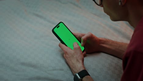 Man using a green screen smartphone on a bed
