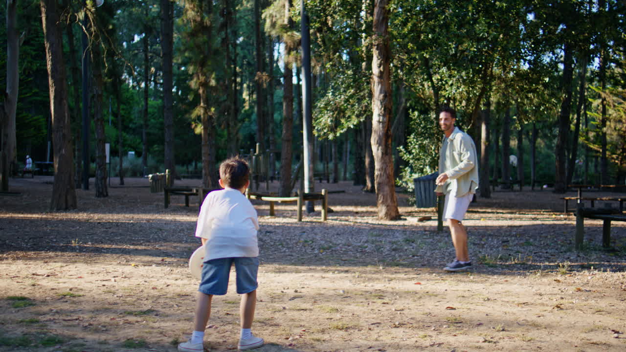 Dad son throwing frisbee in sunny park. Young man little boy having fun together