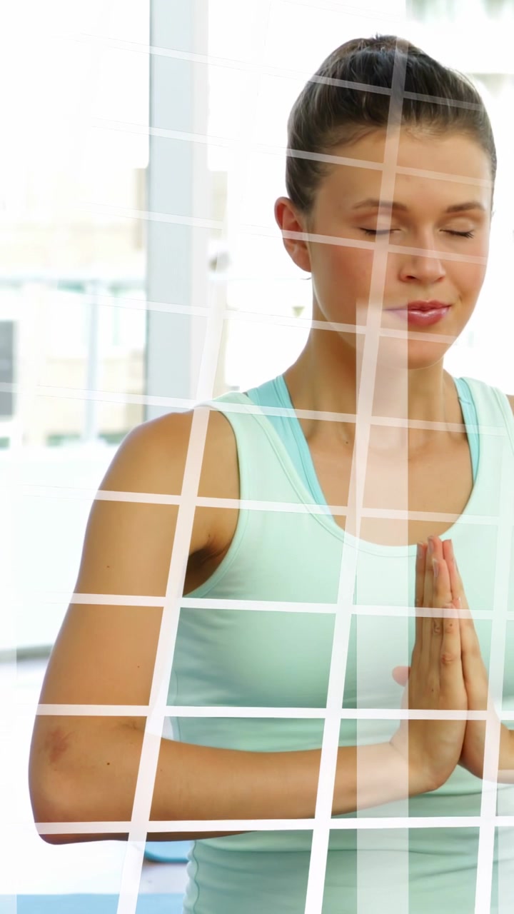 Mujer con las manos en posición de oración, centrando la respiración en un estudio de yoga mientras la cuadrícula de una ventana se proyecta sobre su torso.