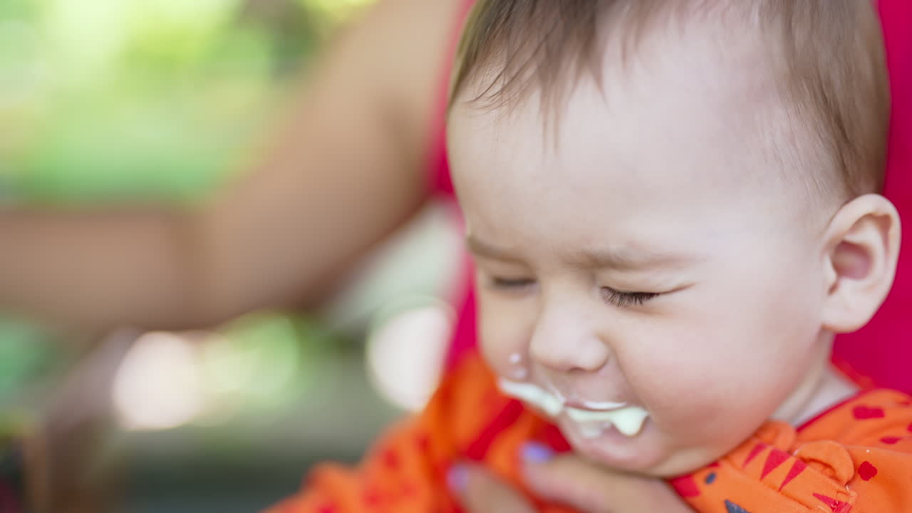 Sweet child opens mouth wide to the full spoon. Beautiful baby closes eyes disliking food and coughs. Close up.