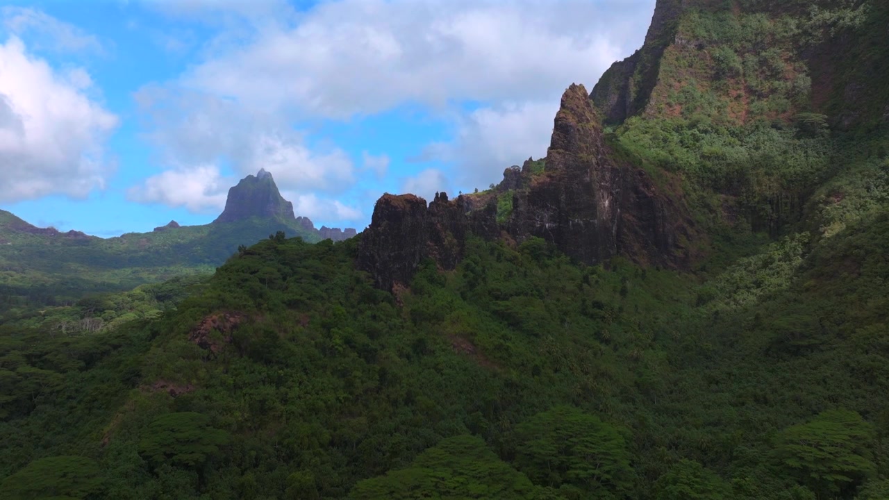 Belvedere utsiktsplats Moorea Tahiti ö Franska Polynesien Mount Toheia Mt Rotui flygfoto drönare frodig grön djungelskog vulkaniska taggiga oländiga bergstoppar solig morgon blå himmel moln uppåtgående rörelse