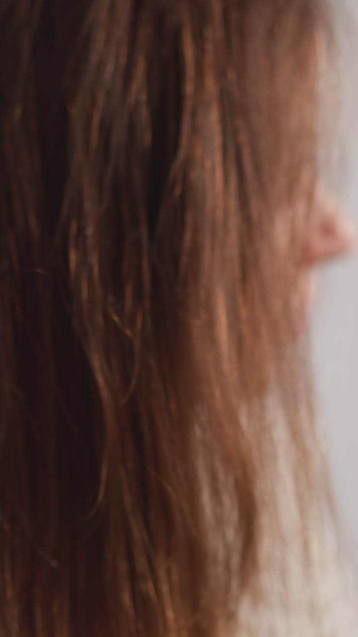 Lady smooths hair after shampooing in bathroom. Attractive woman combs dark hair with massage brush after shower in light toilet slow motion