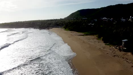 Seaside-homes-overlook-a-tranquil-beach-with-lush-hills-in-the-backdrop,-golden-hour-light