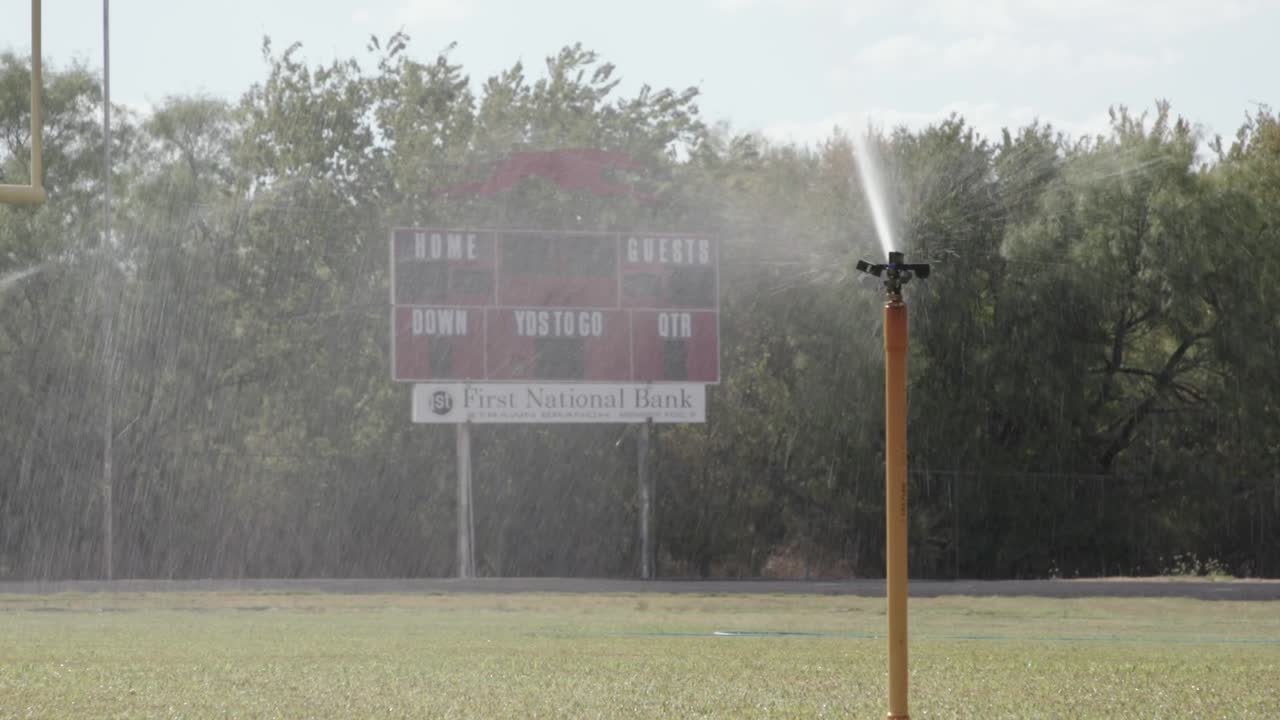 cabezal de rociador rociando agua en un campo de fútbol de una escuela secundaria de texas luces del viernes por la noche