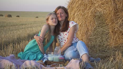 happy family in a wheat field. mother and daughter on a picnic in a wheat field near one of round bales at sunset time