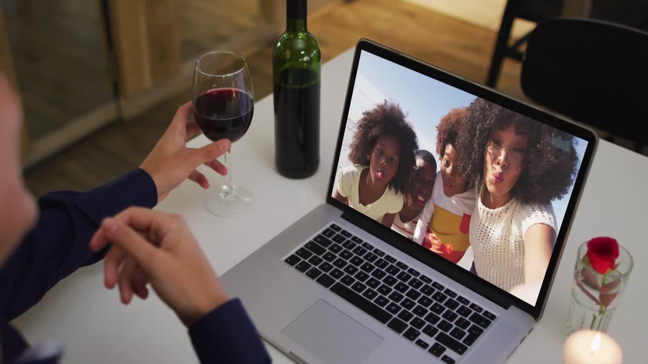 아프리카계 미국인 여성의 중간 섹션은 집에서 노트북으로 비디오 통화를 하는 동안 와인 잔을 들고 있습니다.