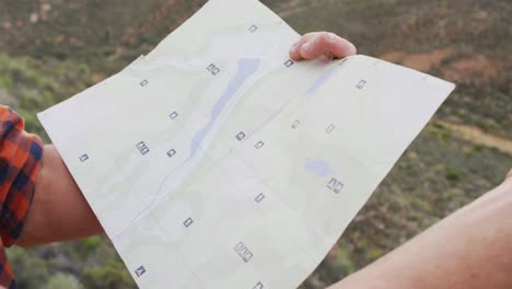 hombre caucásico sobreviviente sentado en el pico de la montaña en el desierto, sosteniendo un mapa