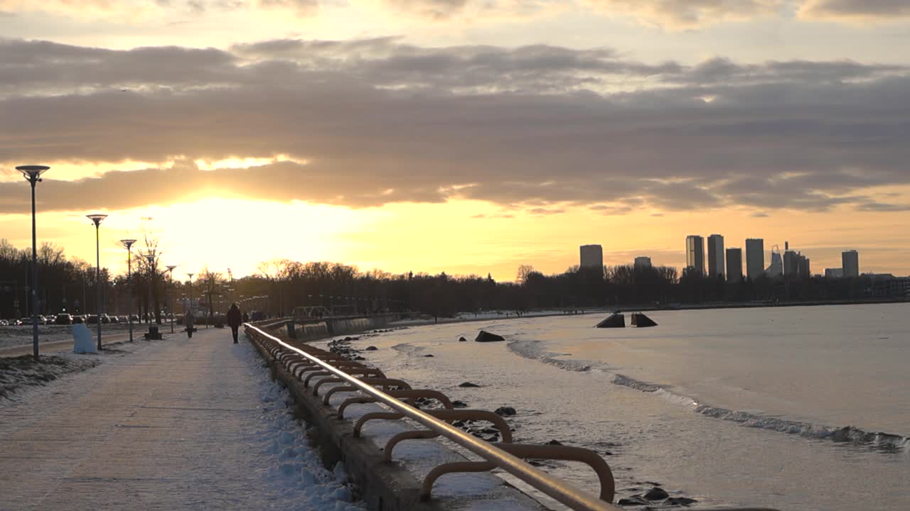 magnífico panorámica de izquierda a derecha imágenes de la silueta de la ciudad de tallin durante un amanecer o puesta de sol que hace que el cielo amarillo dorado y naranja. algunas nubes están en el cielo. olas del mar báltico visto en movimiento a la derecha.